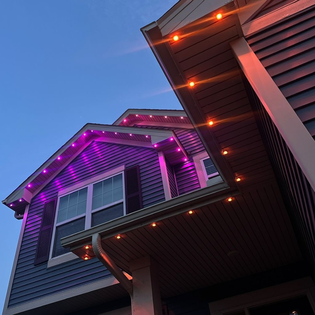 Close-up of purple and warm permanent LED lights along a roofline at dusk